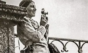 Zofia Chomętowska, z aparatem w dłoni, patrzy w dal. W tle balustrada i jasne niebo.