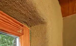 Lehmputz nachteile: raue Textur, die Schmutz anziehen kann, um ein Fenster mit Holzzarge und sichtbarem Putz.