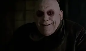 Uśmiechnięty, łysy mężczyzna z ciemnymi kręgami wokół oczu. To wujek Fester z Rodziny Addamsów, znany ze swoich dziwacznych żartów.