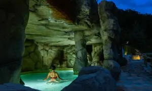 Una mujer disfruta de un relajante spa de noche en una piscina natural rodeada de rocas.