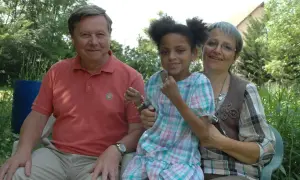 Un homme, une femme et une petite fille souriants, peut-être la famille de Leonard Berducat, profitent d'un moment ensoleillé dans un jardin.