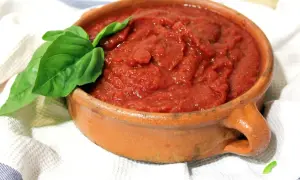 Un cuenco de barro rústico lleno de vibrante salsa de tomate casera, adornado con una hoja de albahaca fresca.