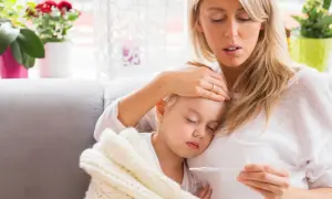 Zmartwiona mama sprawdza temperaturę chorej córki, która śpi otulona kocykiem. Myśli o podaniu Fervex dla dzieci.
