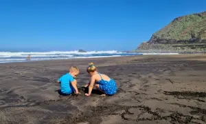 Dzieci bawią się na czarnej plaży, szukając skarbów. Teneryfa atrakcje dla dzieci to raj dla małych odkrywców.