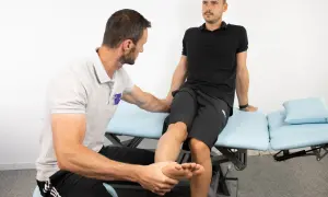 Fysioterapeut utför piriformis syndrom test på patient som sitter på en undersökningsbrits.
