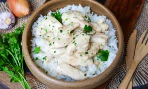 Schmackhaftes Puten Geschnetzeltes in cremiger Sauce auf Reis, garniert mit Petersilie. Daneben Zwiebel und Knoblauch.