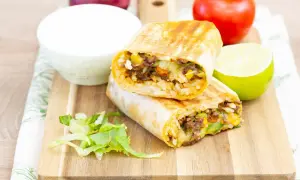Pyszny burrito przepis: dwa połówki burrito z ryżem, mięsem mielonym, kukurydzą i warzywami, podane z limonką i śmietaną.