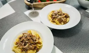 Deux assiettes de pâtes conchiglioni garnies d'une généreuse sauce bolognaise, prêtes à être dégustées avec un verre de vin rouge.