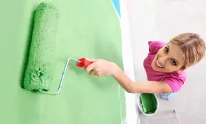 Frauen streichen bei Auszug nach 5 Jahren die Wand grün. Sie lächelt fröhlich, während sie mit der Rolle die Farbe aufträgt.
