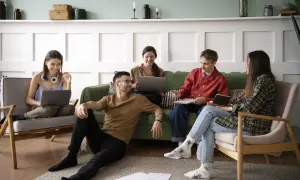 Cinq jeunes discutent et travaillent ensemble dans un salon, une scène typique d'une colocation avec un bail solidaire.