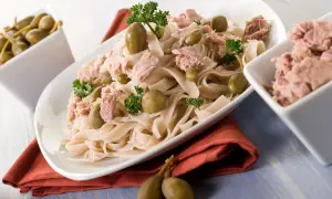 Makaron z kawałkami tonno, oliwkami i kaparami. Obok miseczka z dodatkowym tonno.