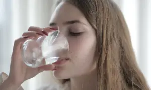 Młoda kobieta pije wodę z kieliszka, wykonując prosty test na odwodnienie.