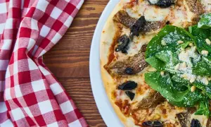 Pizza z rukolą i grzybami na białym talerzu, obok czerwono-biała kraciasta serwetka.