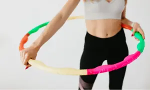 Kobieta w sportowym stroju trzyma kolorową obręcz hula hop. Czy hula hop jest szkodliwe? Nie, to świetna zabawa i trening!