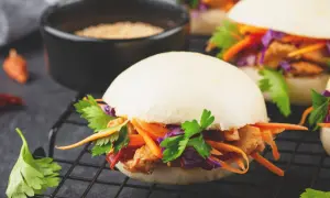 Saftiger bao burger mit Hähnchen, Karotten, Rotkohl und Koriander auf einem Rost.