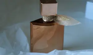 Elegancka butelka perfum Lancome Eclat w kolorze miedzi, ozdobiona brokatową wstążką, otulona delikatnym białym papierem.