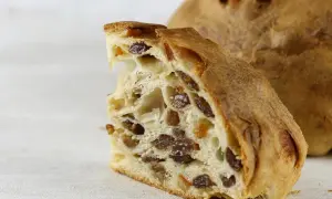 Fetta di pandolce genovese ricetta originale, con uvetta e canditi, su sfondo chiaro.
