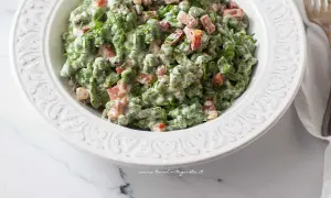 Un piatto di gnocchetti tirolesi verdi, conditi con panna, piselli e speck croccante, guarniti con erba cipollina.