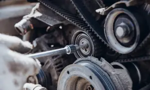 Mano enguantada ajusta la correa de servicio de un motor con una llave de carraca.