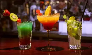 Trzy kolorowe drinki: zielono-czerwony z owocami, pomarańczowo-czerwony w kieliszku oraz zielony mojito.