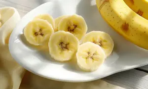 Fette di banana su un piatto bianco, con banane intere sullo sfondo. La banana è astringente o lassativa, a seconda della maturazione.