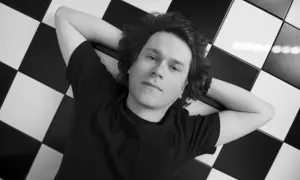 Hubert Humka leży na czarno-białej szachownicy, ręce za głową, w czarnej koszulce.