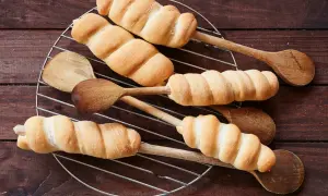 Frisch gebackenes Stockbrot mit frischer Hefe, auf Holzkochlöffeln auf einem Gitterrost arrangiert.