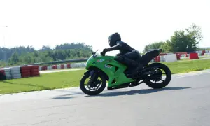 Motocyklista w kombinezonie na zielonym motocyklu ściga się na torze wyścigowym.