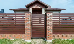 Eleganckie ogrodzenie z klinkieru i brązowych paneli, z solidną bramą wjazdową, stanowi ozdobę posesji.