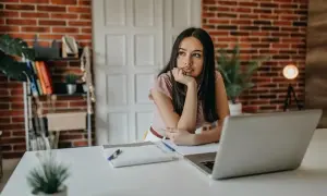 Młoda kobieta siedzi przy biurku, zamyślona, przeżywa kryzys 30 latka. Laptop i notatki leżą przed nią.