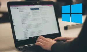 Osoba pisze na laptopie, na ekranie widać artykuł o malowaniu dachu. W tle widnieje niebieskie logo Windows.