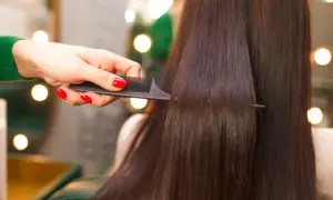 Mano con unghie rosse pettina capelli lisci e scuri, creando un look impeccabile.