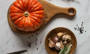 Pomarańczowa dynia muscat na drewnianej desce, obok czosnek, pieprz i zioła. Idealne składniki na jesienną zupę.
