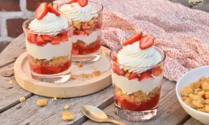 Trois verrines fraise mascarpone facile, garnies de crème fouettée et de fraises fraîches, sur une table en bois.