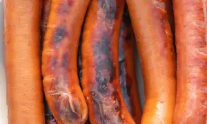 Zbliżenie na kilka grillowanych kiełbasek, niektóre lekko przypalone.