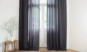 Ciemne zasłony wiszą przy drzwiach balkonowych. Wazon z gałązkami na drewnianym stołku. Jak mierzyć zasłony?