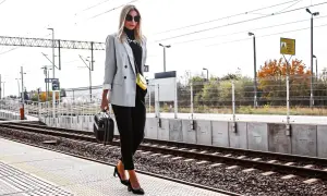 Elegancka szara marynarka damska w stylizacjach na podróż. Kobieta z małą walizką na peronie kolejowym.