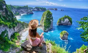 Vue imprenable sur la côte de Bali. Une femme assise au bord d'une falaise admire les îlots verdoyants et l'océan bleu. Idéal pour savoir que faire à Bali.