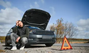 Zmartwiony mężczyzna przy awaryjnym samochodzie z otwartą maską i trójkątem ostrzegawczym. Przerwa w OC? Jak uniknąć kary za brak ubezpieczenia?