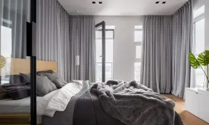 Elegancka sypialnia z dużym łóżkiem, przytulnym futrzanym kocem i szarą zasłoną w oknie, która tworzy przytulną atmosferę.