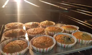 En plåt med nybakade glutenfria muffins i ugnen. Ljuset från ugnen lyser upp de gyllene muffinsarna.