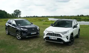 Dwa nowe modele Toyota RAV4 2025, czarny i biały, zaparkowane na trawie nad jeziorem.