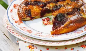 Ein goldbrauner Pfannkuchen mit Kirschen, bestreut mit Zucker, auf einem Teller mit Blumenmuster.