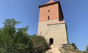 Wieża zamku Melsztyn z polską flagą na szczycie, kamienna podstawa i ceglana nadbudowa.