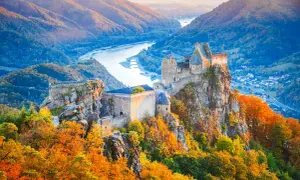 Zamek na skale w dolinie Wachau, otoczony jesiennymi barwami, z rzeką w tle.