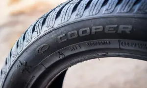 Zbliżenie na bok czarnej opony Cooper z widocznymi oznaczeniami, m.in. rozmiarem 225/55R18 i symbolem płatka śniegu.