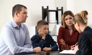 Rodzina z dzieckiem rozmawia z prawnikiem lub kuratorem sądowym. Na stole waga sprawiedliwości.