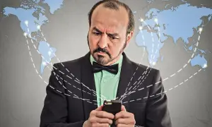 Mężczyzna w garniturze z kokardką patrzy na telefon, zastanawiając się, co to roaming i jak działa globalna sieć.