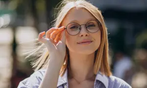 Kobieta w okularach z okrągłymi oprawkami poprawia je palcem.