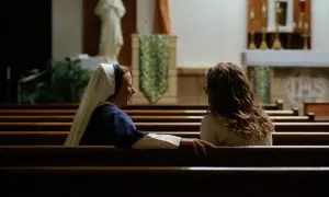 Siostra zakonna rozmawia z młodą kobietą w kościele.